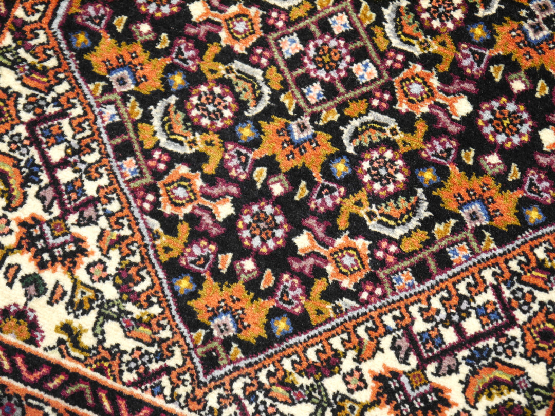 Nahaufnahme des fast schwarzen Feldes im Bidjar Tekab, Herati-Rosetten und -Blätter in Orange, Gold und Aubergine neben dem Elfenbein-Eckzwickel