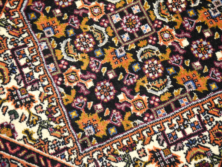 Nahaufnahme des fast schwarzen Feldes im Bidjar Tekab, Herati-Rosetten und -Blätter in Orange, Gold und Aubergine neben dem Elfenbein-Eckzwickel
