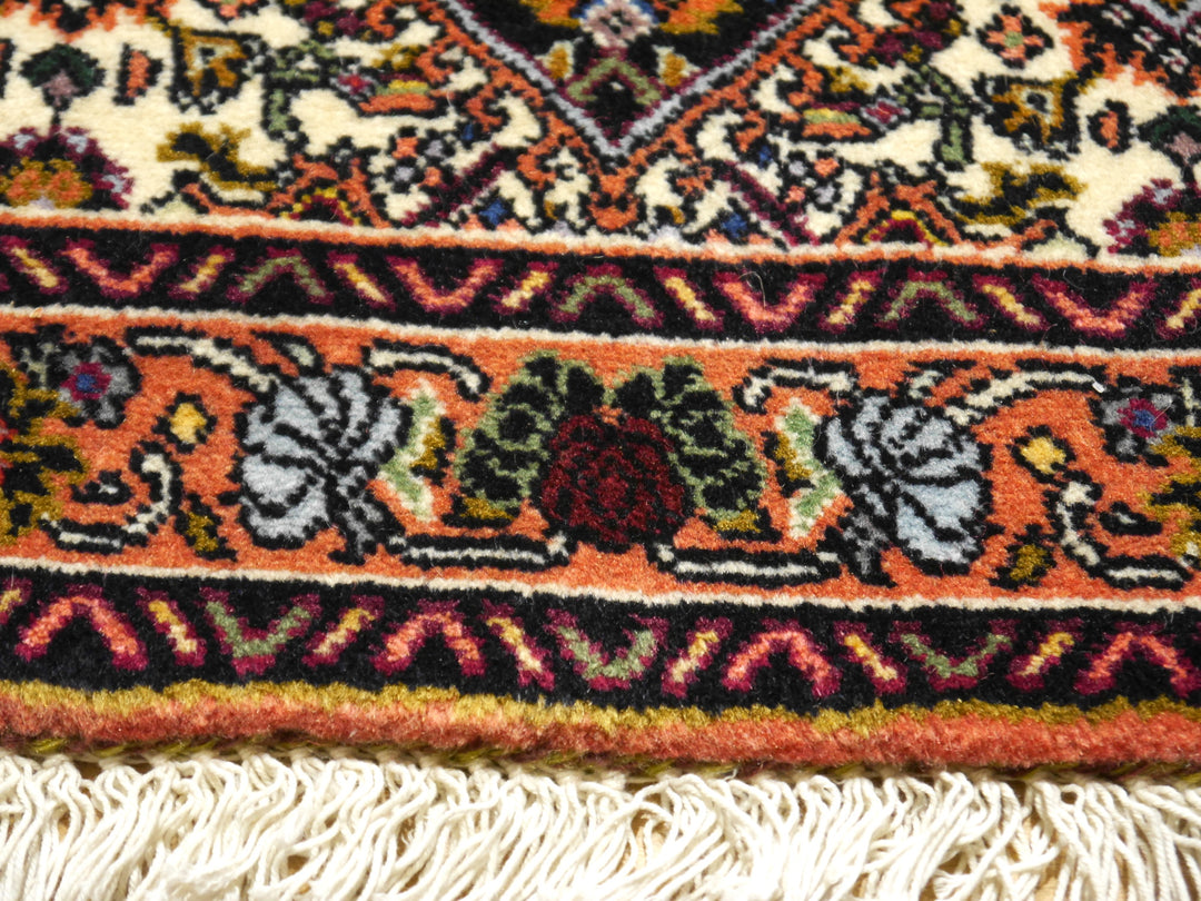 Bordürendetail des Bidjar Tekab: Elfenbein-Eckzwickel, marineblaue Zackenstreifen und Terrakotta-Hauptbordüre mit Rosen über der flach gearbeiteten Fransenkante