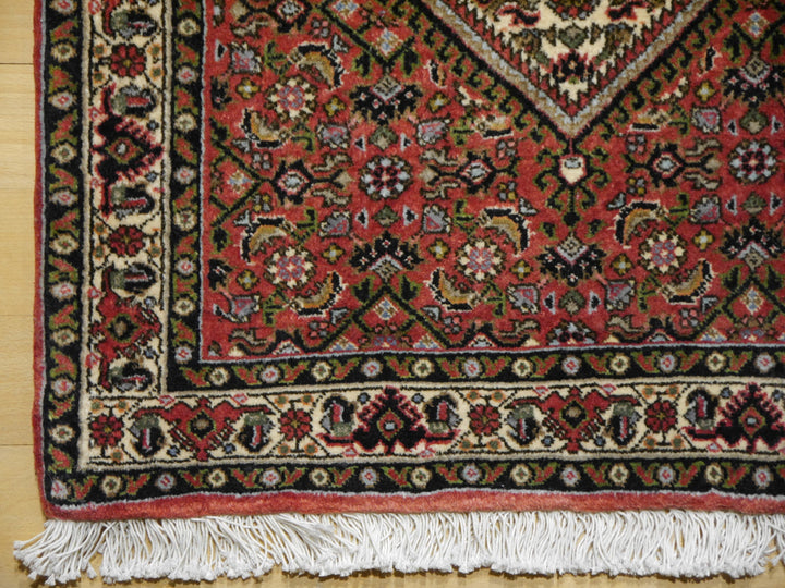 Ecke des Bidjar Tekab auf Holzboden: Elfenbein-Hauptbordüre mit roten Palmetten und Boteh, dunkelblaue Innenbordüre und Baumwollfransen