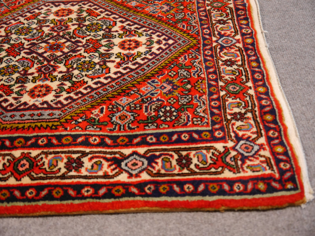 Corner detail of the Tekab Bidjar runner: ivory main border with red rosettes and pink palmettes, navy guard stripes and flat-finished selvedge